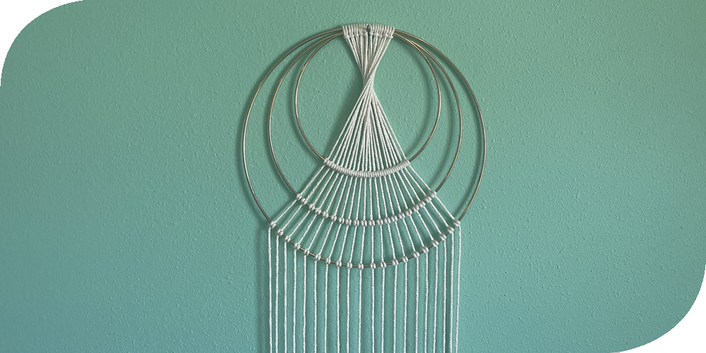 Macrame triple ring wall hanging on an aqua wall.